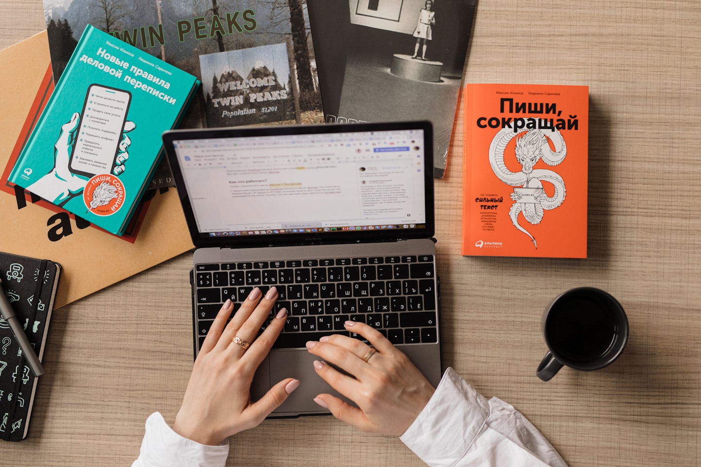Hände tippen auf einem Laptop, umgeben von Büchern und Kaffee.