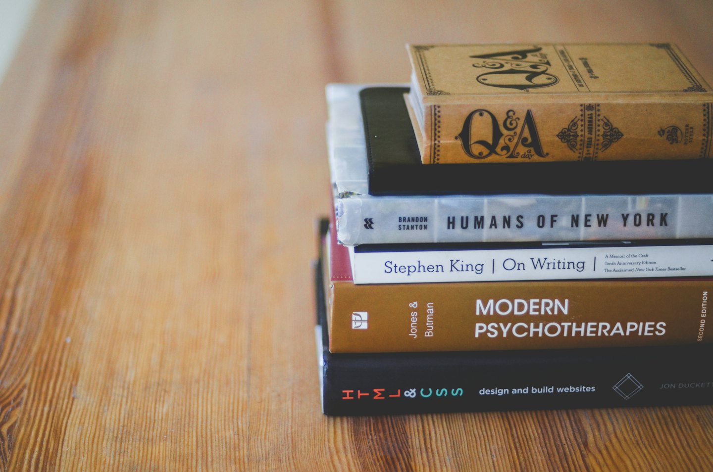 Fünf gestapelte Bücher auf einem Holztisch.